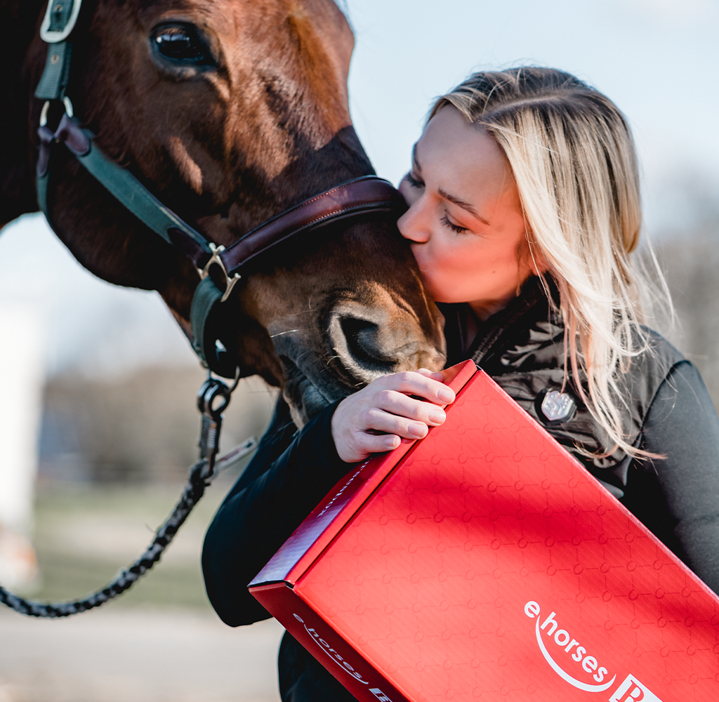 Junge Frau hält ehorses Box in der Hand und küsst dabei ihr Pferd